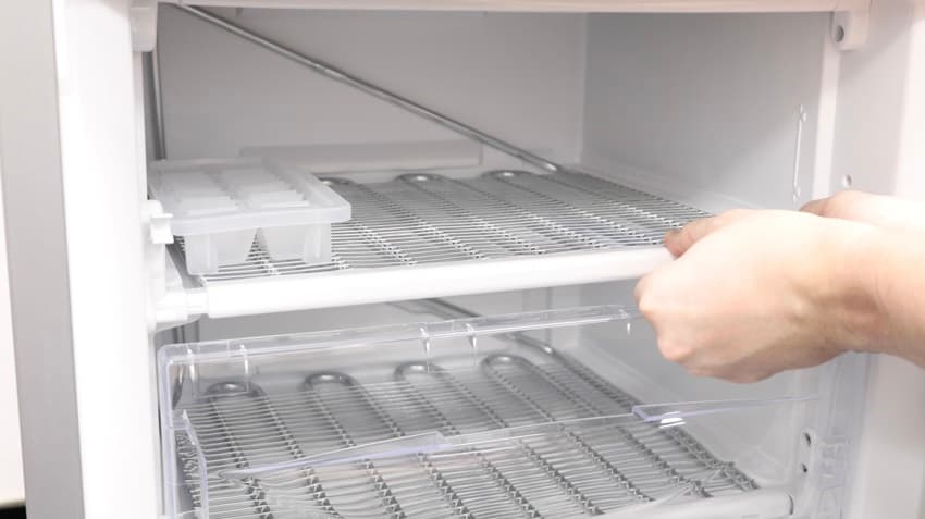 Hands replacing a shelf inside a fridge freezer